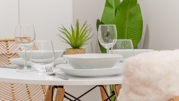 A dining table set with white plates, bowls, and glasses, accompanied by a fork and knife, and a small potted plant.