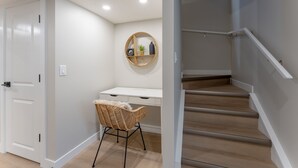 A modern interior with a white desk, wicker chair, and a wooden staircase.