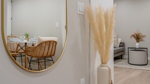 A dining area with a round mirror, wicker chairs, a table set with plates and glasses, and a vase with pampas grass.
