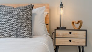 A neatly made bed with patterned pillows, a bedside table with a wooden heart decoration, and a modern lamp.