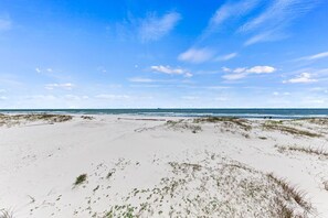 Une plage de sable blanc bordée de dunes, un ciel bleu azur et l’océan en toile de fond.