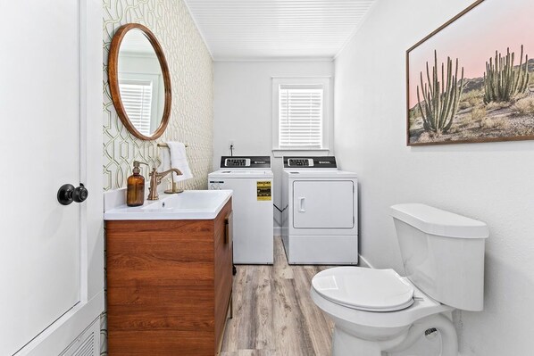 Un baño pequeño con tocador de madera, lavamanos, inodoro y lavadora.
