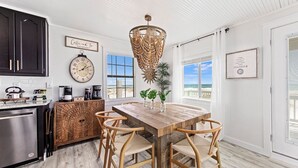 A kitchen with a wooden table, chairs, a clock, and a view of the ocean. - Lux Beachfront House*Private*Fully Loaded*Firepit (Gulf Shores)
