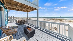 A wooden deck with a fire pit, outdoor furniture, and a view of the beach. - Lux Beachfront House*Private*Fully Loaded*Firepit (Gulf Shores)