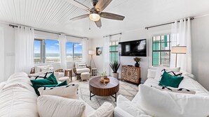 A spacious living room with a ceiling fan, large windows, a flat-screen TV, and a cozy seating area. - Lux Beachfront House*Private*Fully Loaded*Firepit (Gulf Shores)