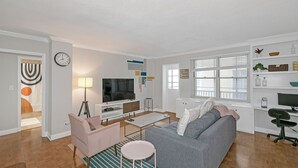 A modern living room with a grey sofa, a pink armchair, a coffee table, and a TV on a white stand. - 21 first floor cozy condo in the center of DT Atlanta (Atlanta)