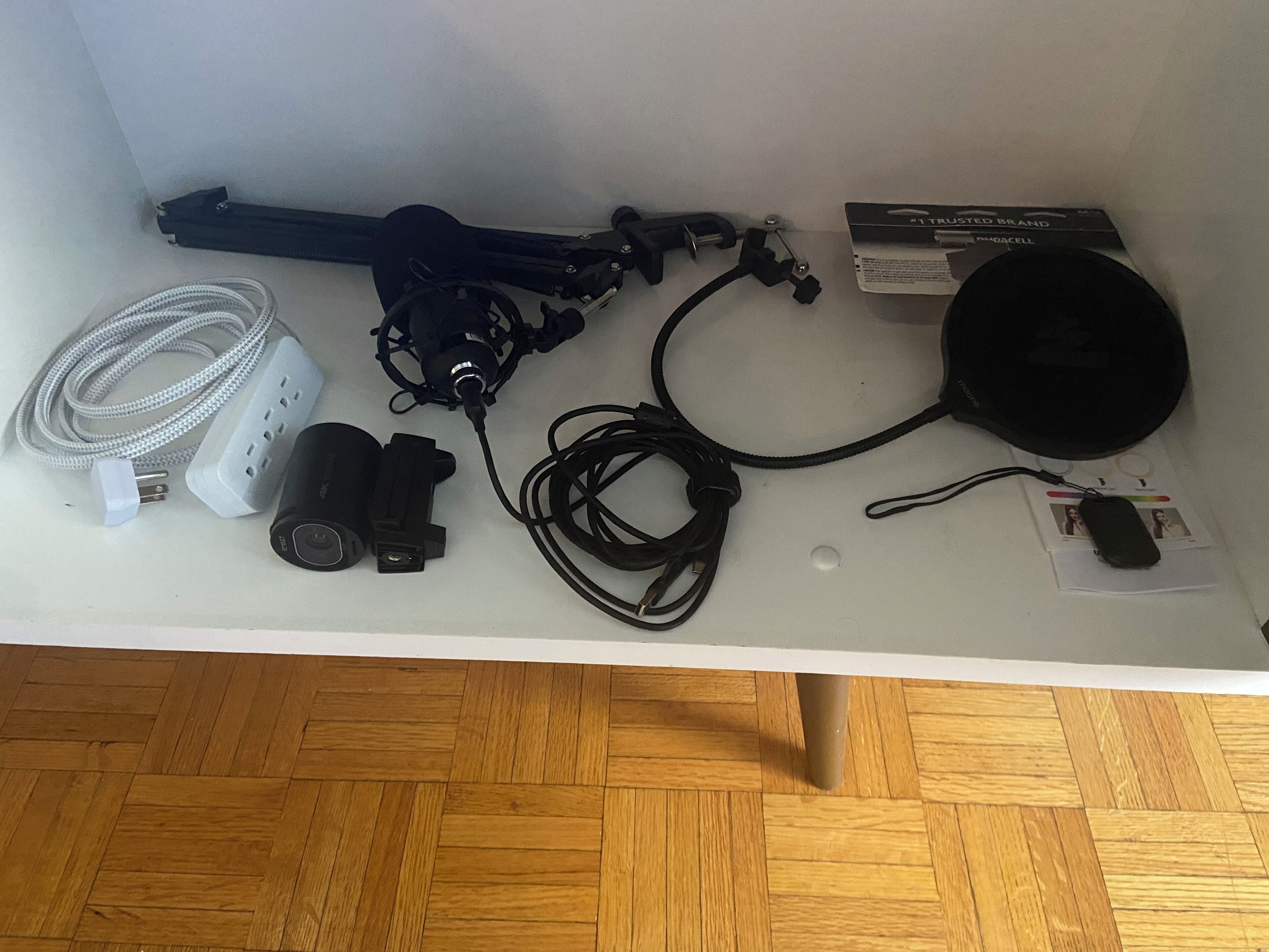 A white table with various electronic devices and cables, including a black power adapter, a white cable, and a black circular object.