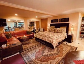 A bedroom with a large bed, a red sofa, a coffee table, and a TV in the background.
