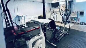 A gym with exercise equipment, a television, and a brick wall.