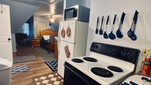 A compact kitchen with a stove, microwave, and refrigerator. There are kitchen utensils hanging on the wall and a checkered rug on the floor.