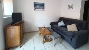 Ein Wohnzimmer mit einem dunkelgrauen Sofa, einem Holztisch, einem kleinen Holzschrank und einem Fernseher auf einem Schrank.