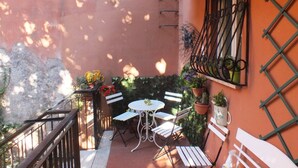 Eine kleine Terrasse im Freien mit Tisch und Stühlen, umgeben von Blumentöpfen und einem dekorativen Metallgitter.