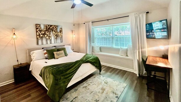 A bedroom with a bed, a ceiling fan, a window with curtains, a wall-mounted TV, and a bedside table. - 3 Bdr/2 Bth home between Katy and Houston close to HWY 10 and Green house  (Katy)