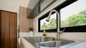 Een moderne keuken met een dubbele spoelbak, houten kastjes, een potplant en een raam met uitzicht op bomen.