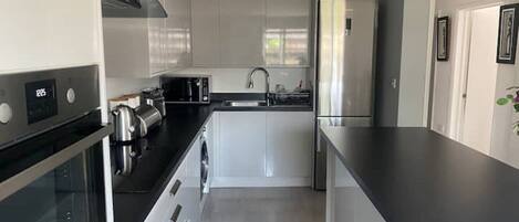 A modern kitchen with white cabinets, a black countertop, stainless steel appliances, and a built-in oven.