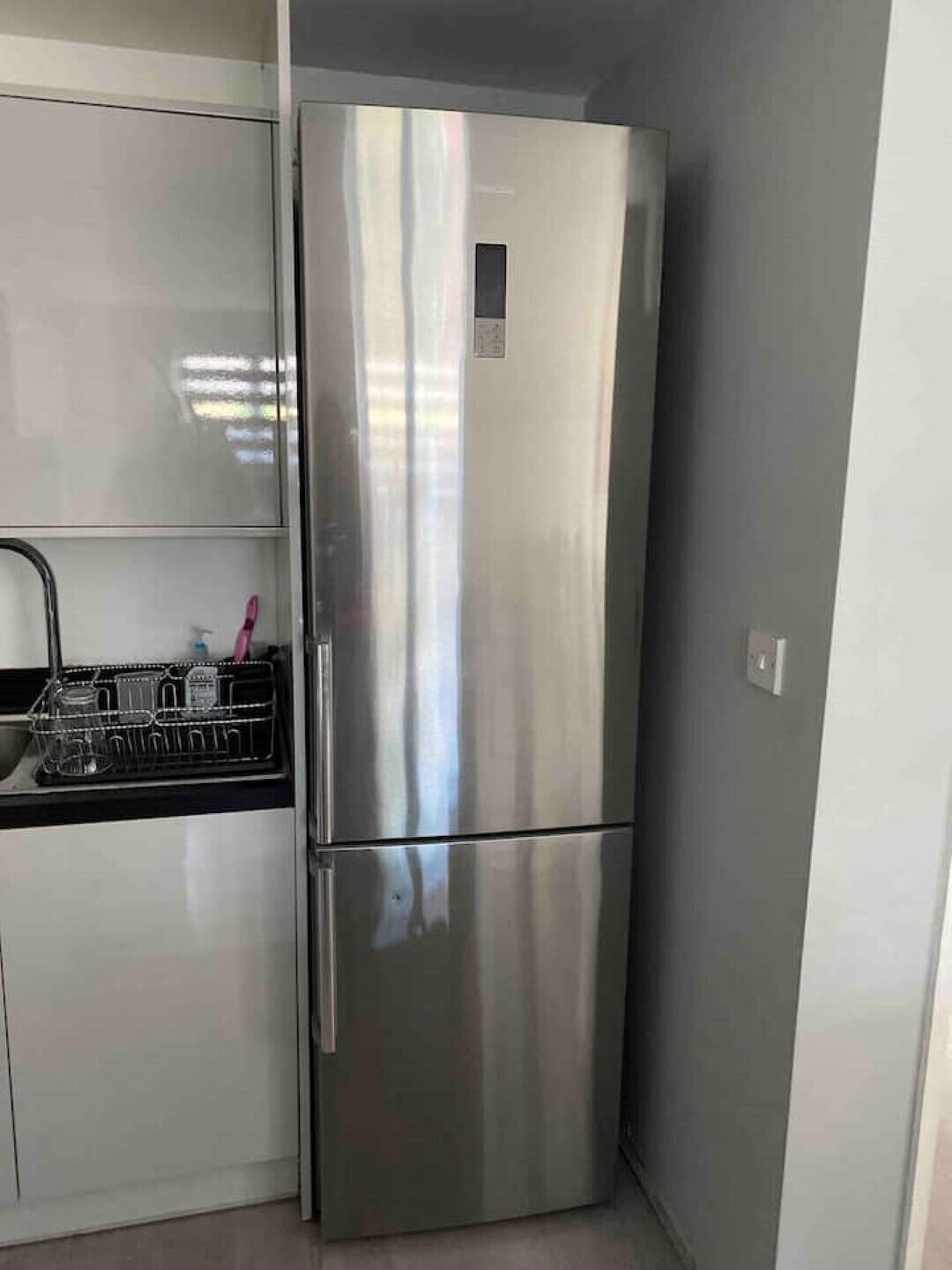 Un refrigerador de acero inoxidable en una cocina con mostrador negro y un escurreplatos.