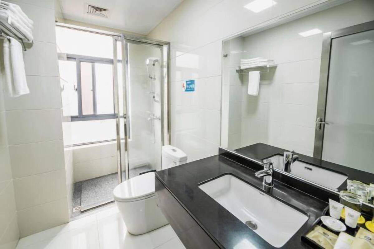 A modern bathroom with a glass shower enclosure, a black countertop, and a large mirror.