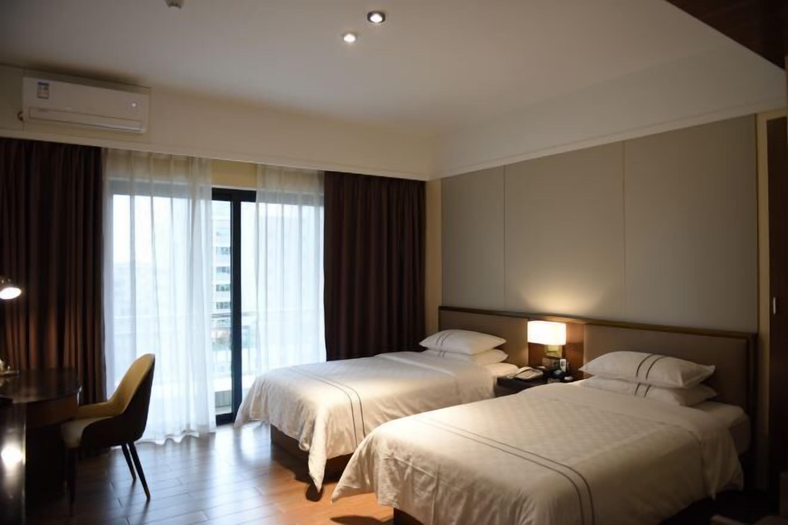 Habitación de hotel con dos camas, un escritorio, una silla y un ventanal con cortinas.
