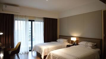 Habitación de hotel con dos camas, un escritorio, una silla y un ventanal con cortinas.