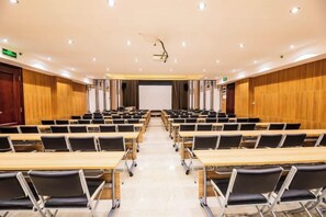 Un salón de conferencias con mesas y sillas dispuestas en filas, una pantalla de proyector y una pared de madera.