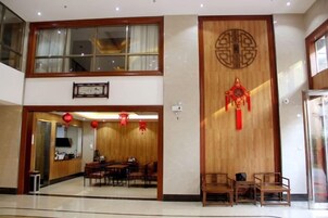 Un hall de hotel con un mostrador de recepción de madera, una zona de estar y una gran pared con decoraciones tradicionales.