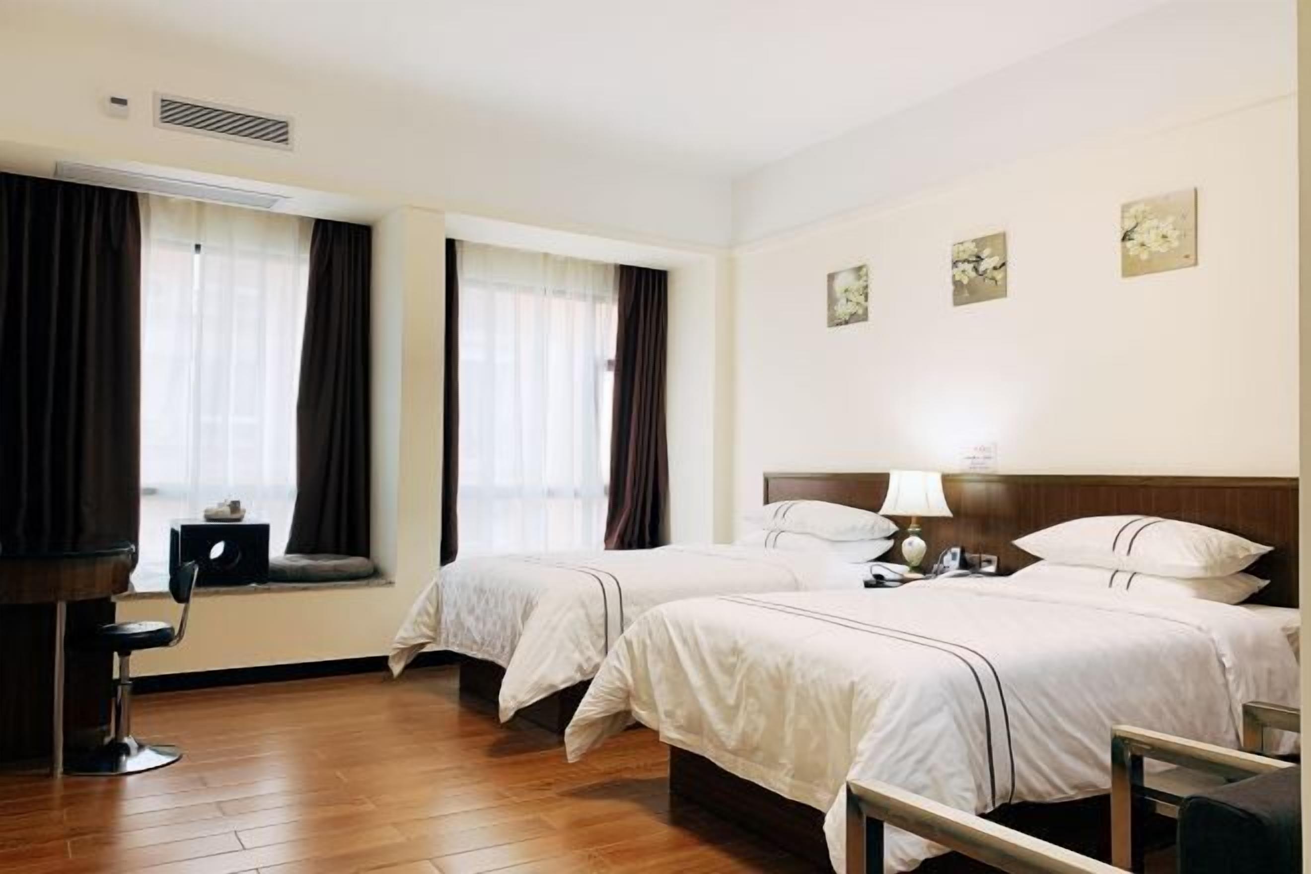 A hotel room with two beds, a desk, and a chair. There are curtains on the windows, and artwork on the walls.