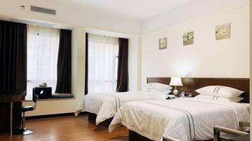 A hotel room with two beds, a desk, and a chair. There are curtains on the windows, and artwork on the walls.