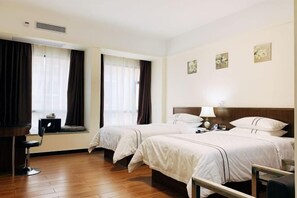 Habitación de hotel con dos camas, un escritorio y una silla. Hay cortinas en las ventanas y obras de arte en las paredes.