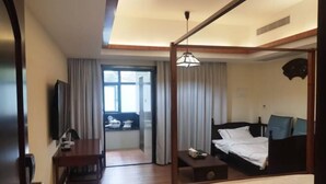 Habitación de hotel con cama, mesita de noche, escritorio con silla, televisión y ventana con cortinas.