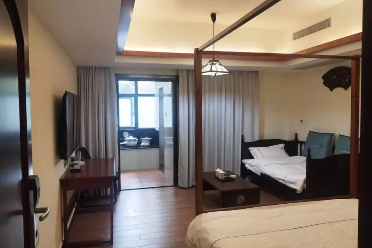 A hotel room with a bed, bedside table, a desk with a chair, a television, and a window with curtains.