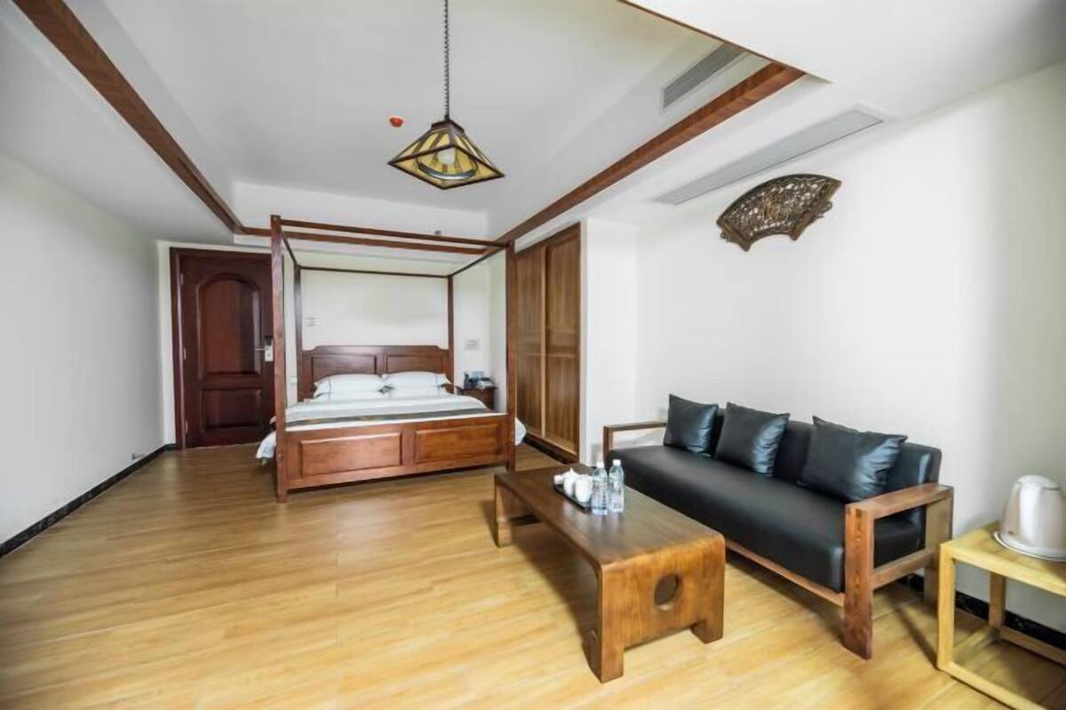 A bedroom with a four-poster bed, a wooden coffee table, a black leather sofa, and a small side table.