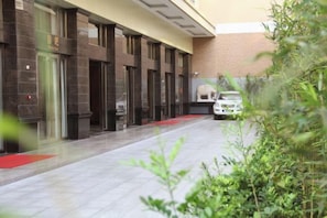 A hotel entrance with a red carpet, a white car parked inside, and a brick wall.