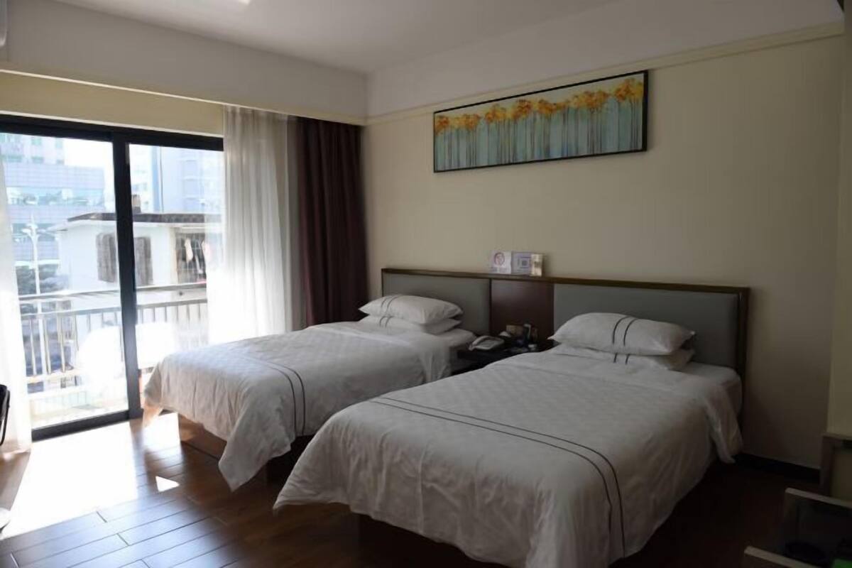 A hotel room with two beds, a large window, and a painting on the wall.