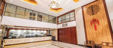 Un hall de hotel con mostrador de recepción, una puerta de madera grande con un emblema decorativo y un candelabro.