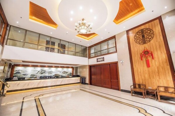 A hotel lobby with a reception desk, a large wooden door with a decorative emblem, and a chandelier.