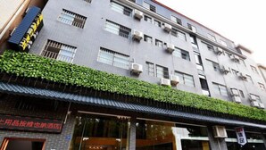 A multi-story building with a brick facade, air conditioning units, and a green ivy-covered awning. - Fenglai Holiday Hostel (Foshan)