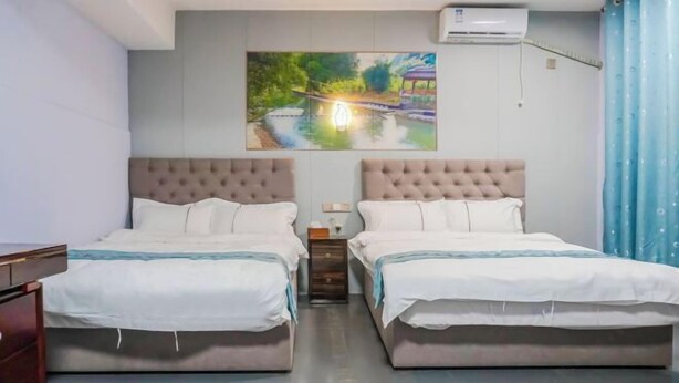 A hotel room with two beds, a painting on the wall, an air conditioning unit, and a blue curtain. - Fenglai Holiday Hostel (Foshan)
