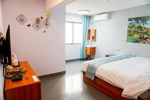 A hotel room with a bed, a desk with a computer, a TV, a window with curtains, a bathroom with a mirror and sink, and a painting on the wall. - Fenglai Holiday Hostel (Foshan)