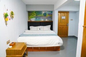 A bedroom with a bed, a wooden bedside table, a wall-mounted shelf with decorative items, a door, and a painting above the bed. - Fenglai Holiday Hostel (Foshan)