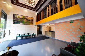 A hotel lobby with a reception desk, seating area, and a staircase leading to an upper level. - Fenglai Holiday Hostel (Foshan)