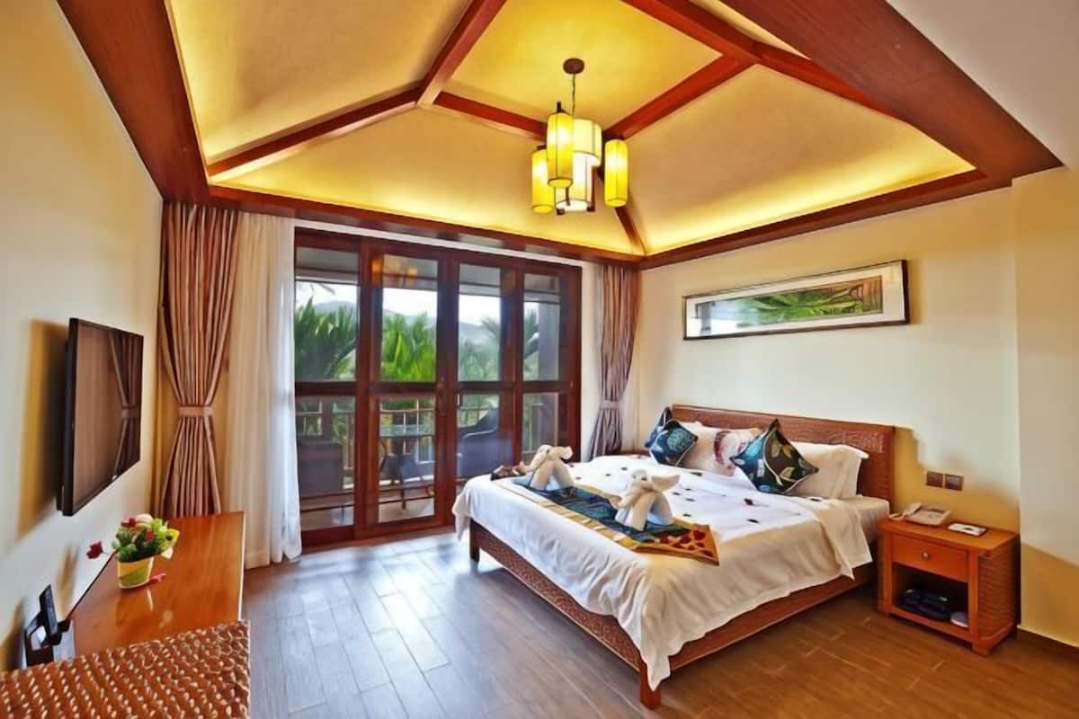 A bedroom with a bed, bedside table, nightstand, and a large window with curtains.