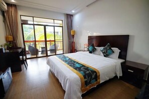 Une chambre d’hôtel avec un grand lit, un bureau et une chaise. Elle dispose d’un balcon avec vue sur les palmiers.