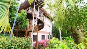A multi-story building with a circular balcony, surrounded by lush greenery and tropical plants.