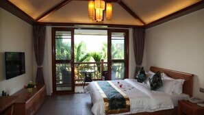 A bedroom with a large bed, a wooden headboard, a bedside table, a TV, and a balcony with a view of greenery.