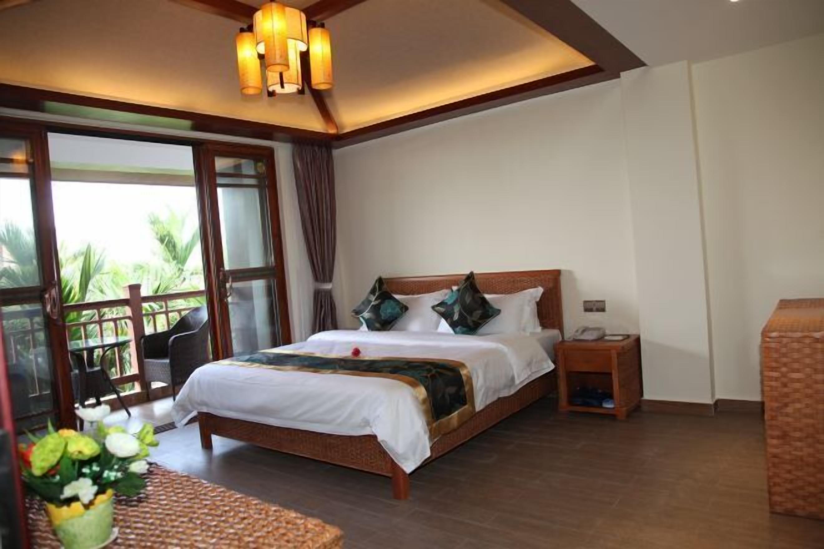 A hotel room with a large bed, a bedside table, a chair, and a view of the outdoors.