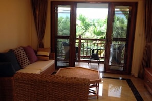 A room with a sofa, a wicker chair, and a glass door leading to an outdoor area with a table and chairs.
