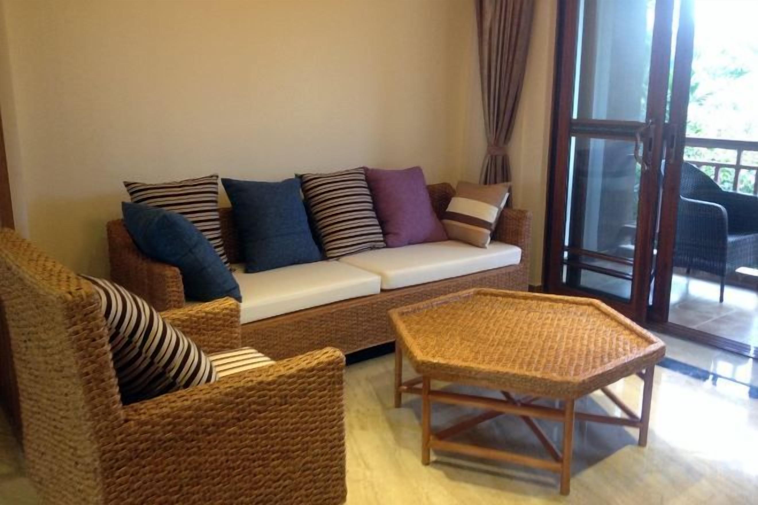 A wicker sofa with cushions, a wooden coffee table, and a glass door leading to an outdoor area.