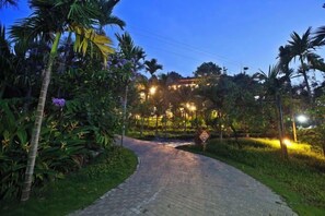 A paved pathway leading to a building with illuminated windows, surrounded by lush greenery and palm trees. - Yabulun Pastoral Leisure Villa (Baoting)