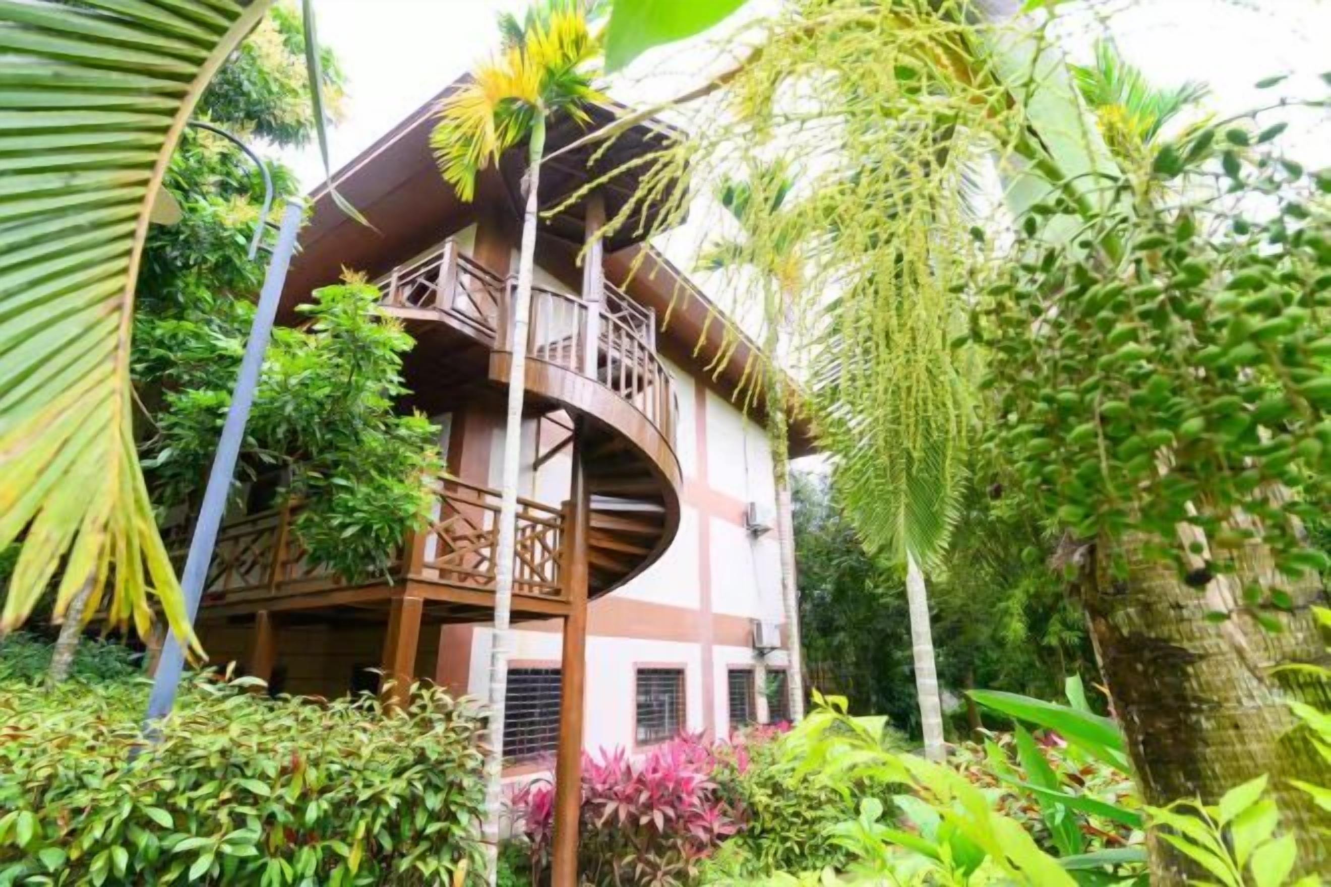 Un bâtiment à deux étages doté d’un balcon, entouré d’une végétation luxuriante.