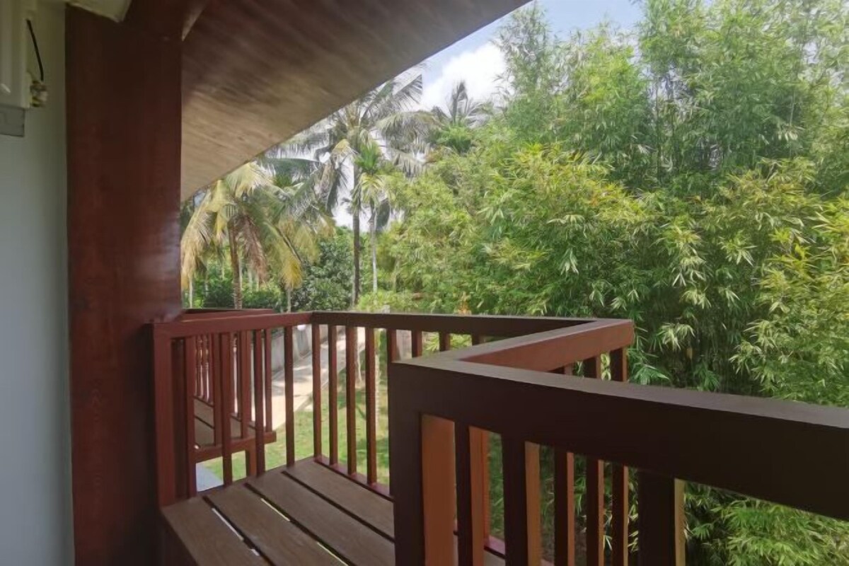 Un balcon en bois offrant une vue sur une végétation luxuriante et des palmiers.